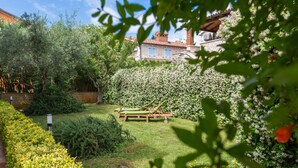Un jardin avec un banc en bois, un mur de briques et, au fond, un bâtiment avec un toit rouge.