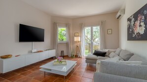 Un salon doté d’un téléviseur à écran plat, d’un canapé blanc et d’une table basse sur laquelle est posé un vase.