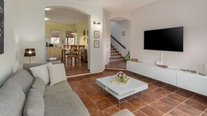 Un salon avec un canapé, une table basse et un téléviseur. Un escalier mène à un espace repas comprenant des chaises et une table.