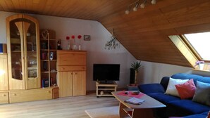 Ett ombonat vardagsrum i loftstil med ett träpanelat tak, en blå soffa, ett träskåp och en tv.