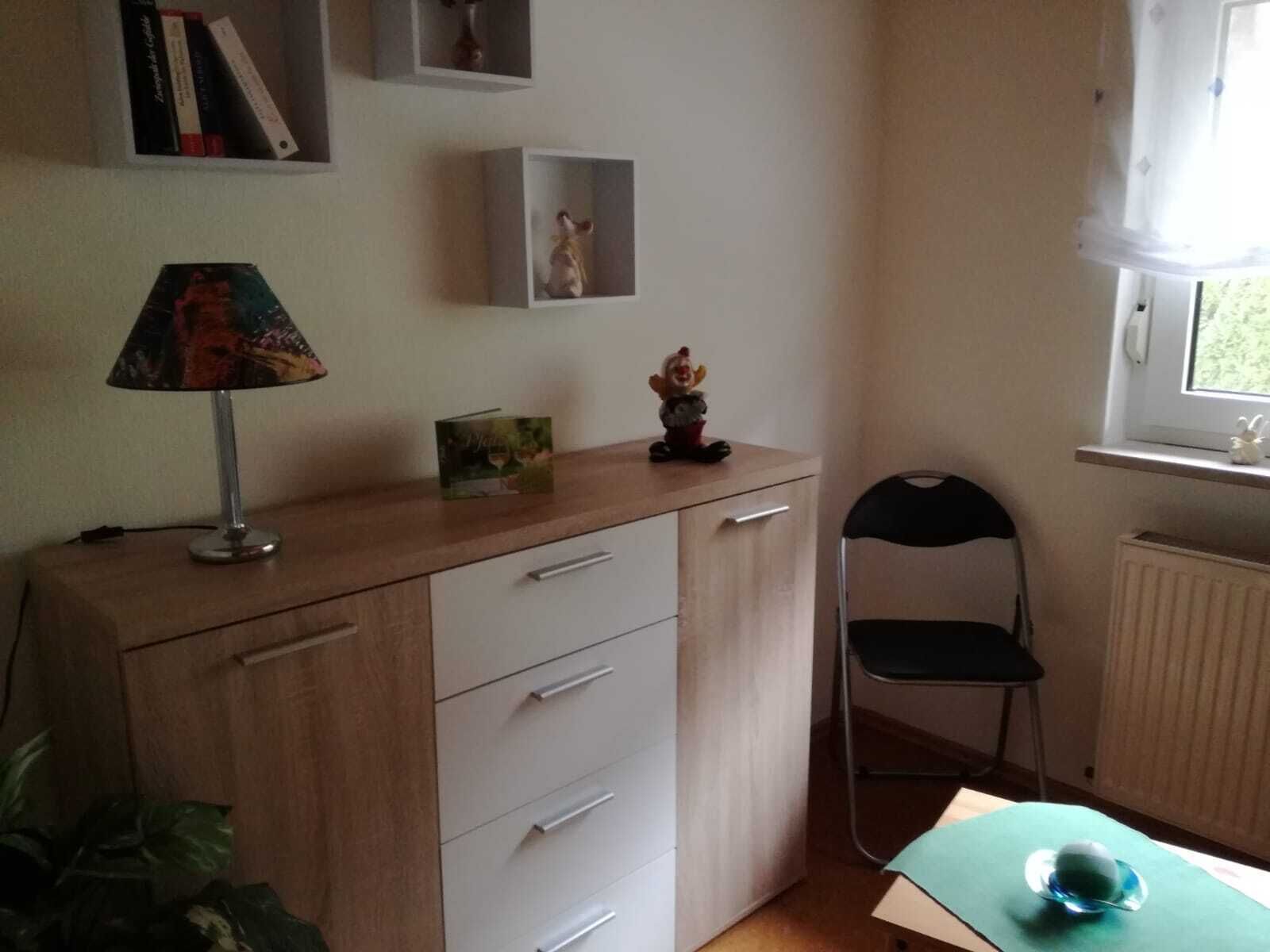 Una habitación con escritorio de madera, una silla, un radiador y una ventana que da a zonas verdes.