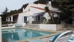 A villa with a swimming pool, outdoor seating, and a stone wall.