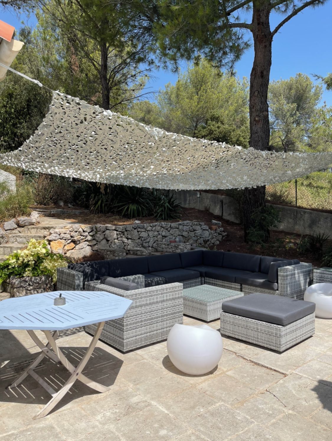 An outdoor seating area with a stone wall, wicker furniture, and a white umbrella.