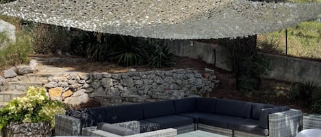 Un área de estar al aire libre con pared de piedra, mobiliario de mimbre y un paraguas blanco.