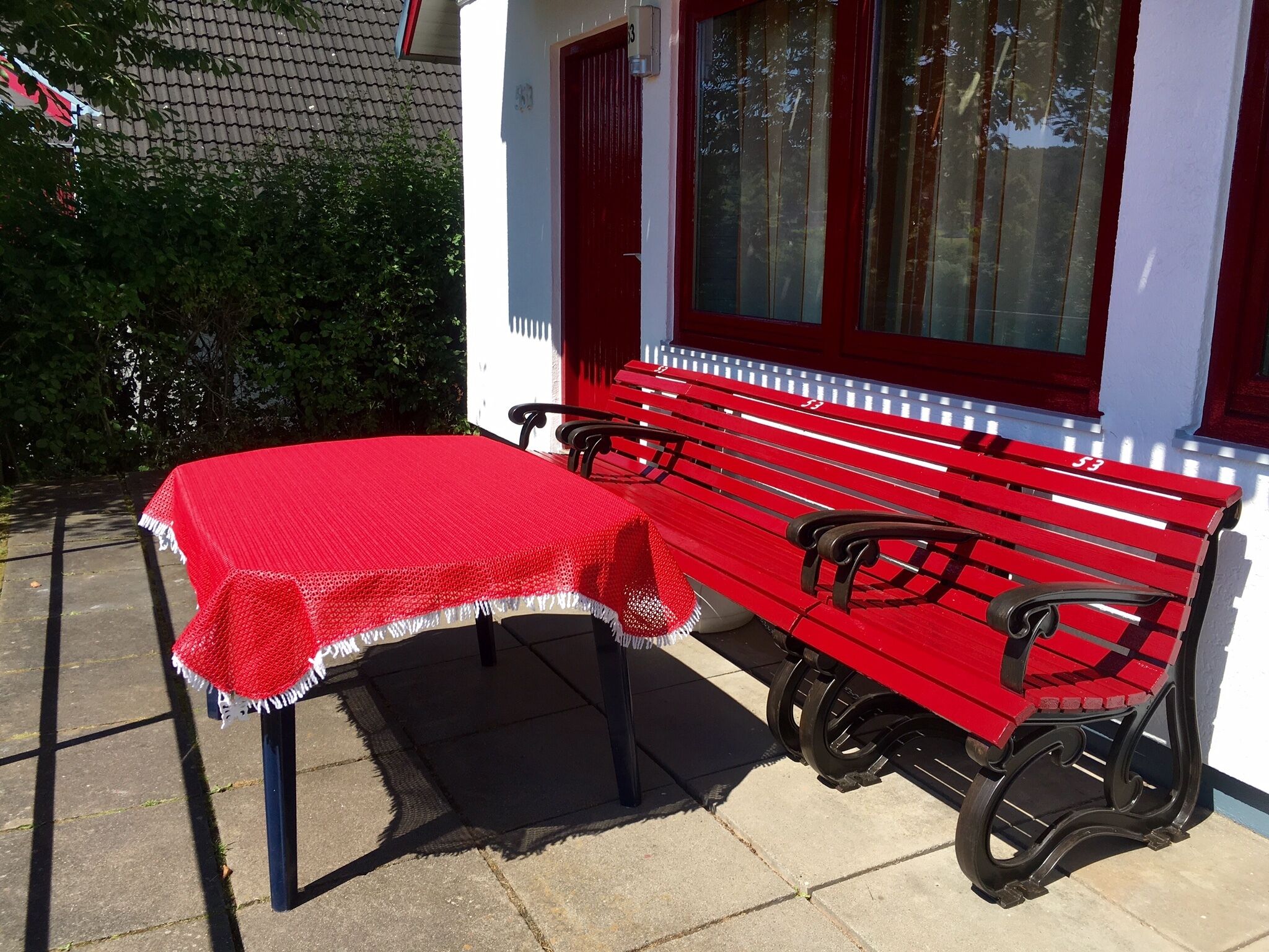 Un banc et une table rouges sont placés à l’extérieur d’un bâtiment à la façade blanche, agrémentée de touches de rouge.