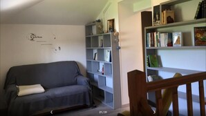 Un salón con un sofá gris, una estantería llena de libros y objetos decorativos, y una pared blanca con un logotipo.