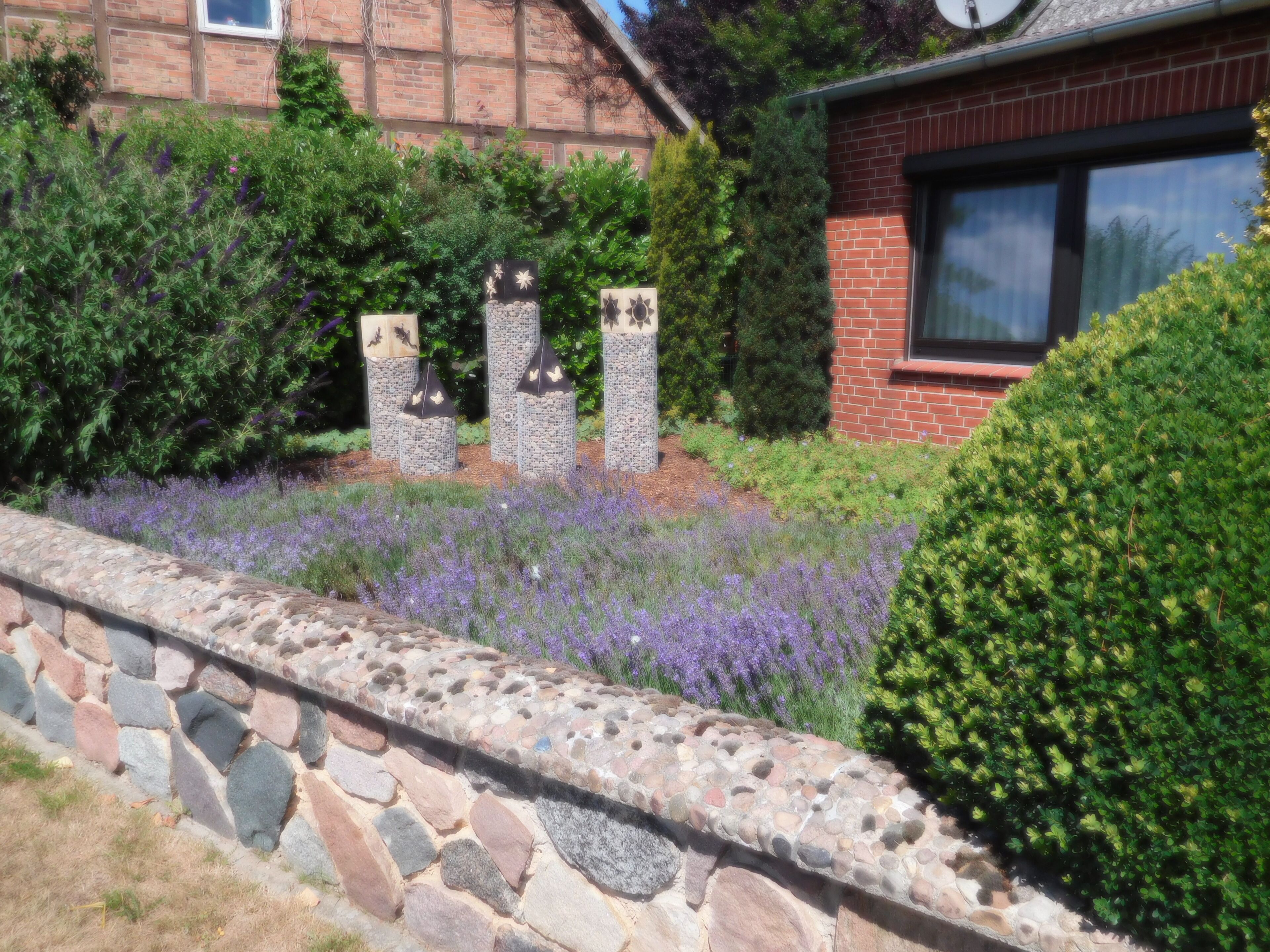 A stone wall with a garden featuring lavender and various shrubs.