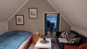 A cozy room with a bed, a sofa, a small table, and a window with curtains. - You will find relaxation and a peaceful idyll here in the Apartment-Feldsteingarten  (Luckau (Wendland))