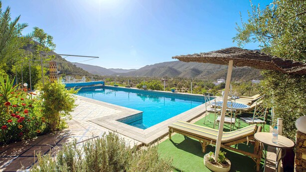 Ein Schwimmbad mit Bergblick, umgeben von Grünflächen und Gartenmöbeln.