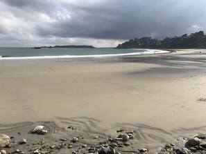 A beach with a rocky foreground, a sandy shore, and a distant view of a coastline with buildings.