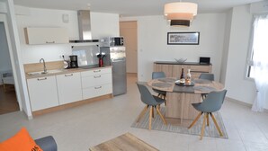 A modern kitchen with white cabinets, a built-in oven, and a microwave. There is a dining area with a wooden table and four chairs. - Apartment *** approved 2018 - Trestraou Beach (Perros-Guirec)