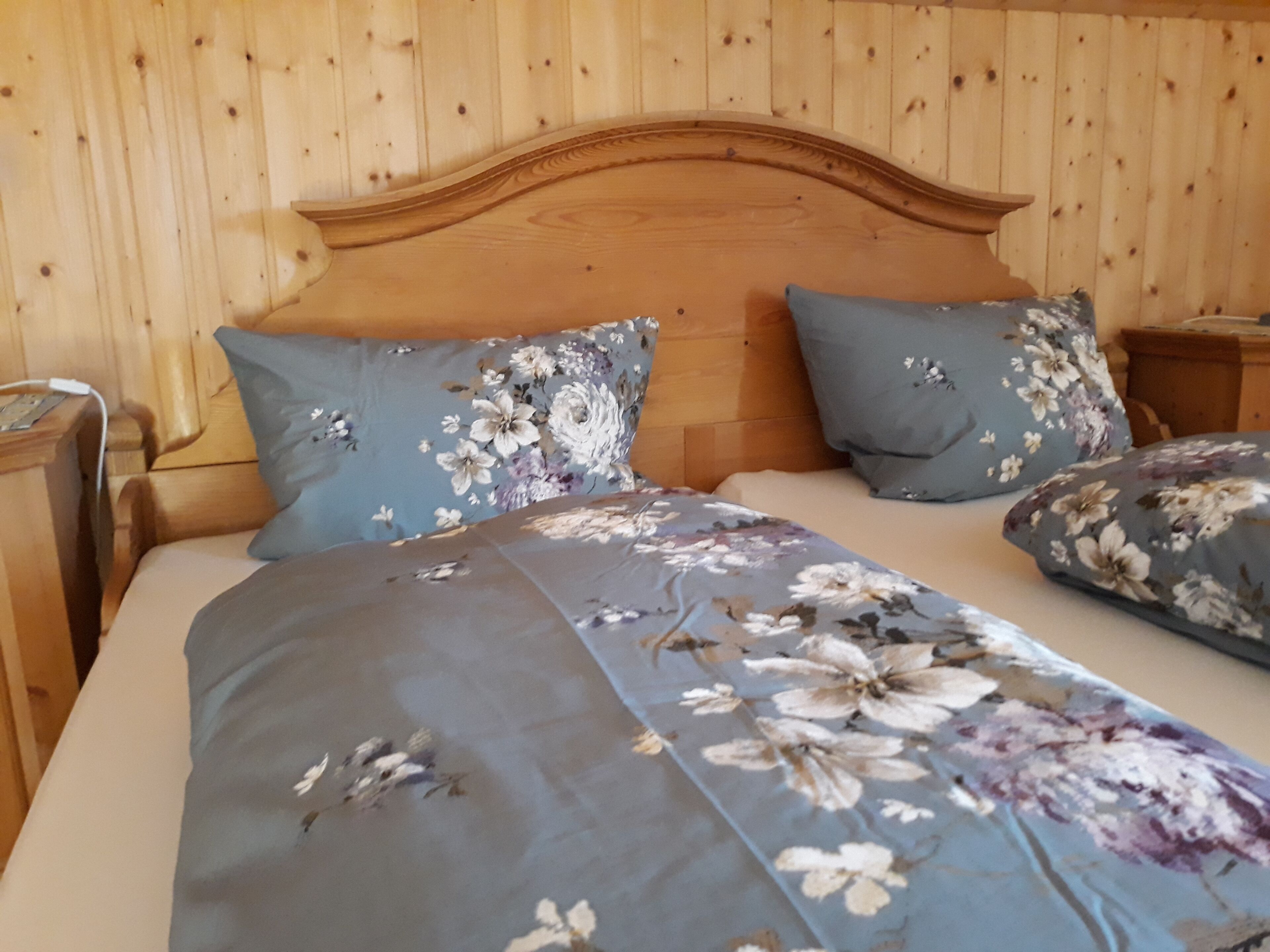 Ein Zimmer mit Holzwänden und einem Bett mit blumigem Bettzeug.