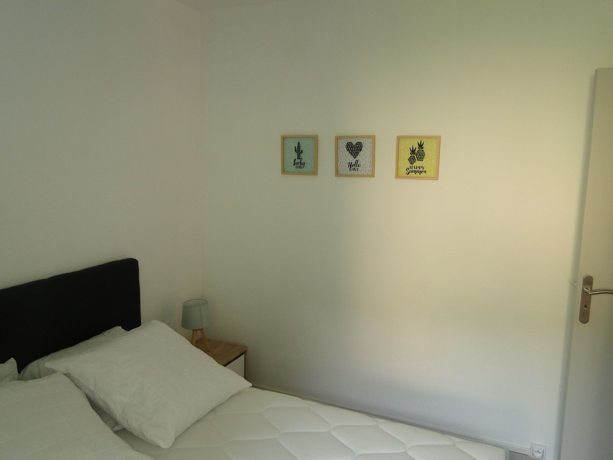 Un dormitori amb un llit, una tauleta de nit i tres quadres al mur.
