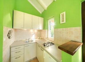 Een kleine keuken met witte kastjes, een gasfornuis, een spoelbak en een raam voor natuurlijk licht.