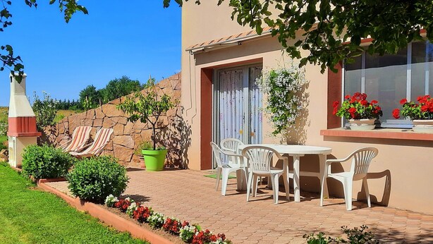 Une terrasse avec une table et des chaises, un pot de fleurs et un mur en pierre.