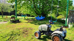 Une tondeuse à gazon se trouve dans une zone herbeuse, à proximité d’une balançoire et de plantes en pot.