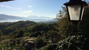 Uitzicht vanuit een overdekt gebied met een hangende lantaarn, op een bergachtig landschap met weelderige begroeiing en een heldere lucht.