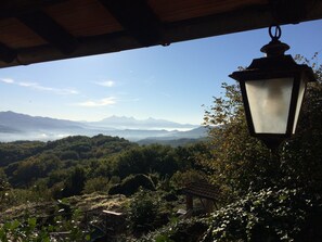 A view from a covered area with a hanging lantern, overlooking a mountainous landscape with dense greenery and a clear sky.