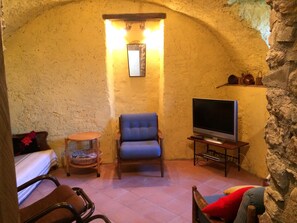 A cozy room with a stone wall, a blue armchair, a wooden side table with a TV, and a small round table with a basket.