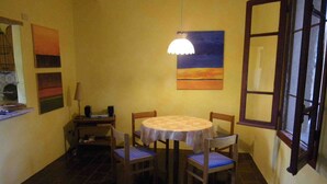 Een eethoek met een ronde tafel, vier stoelen, een lamp en een schilderij aan de muur.