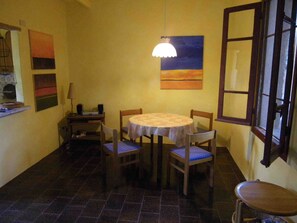 A dining area with a round table, four chairs, a lamp, and a painting on the wall.