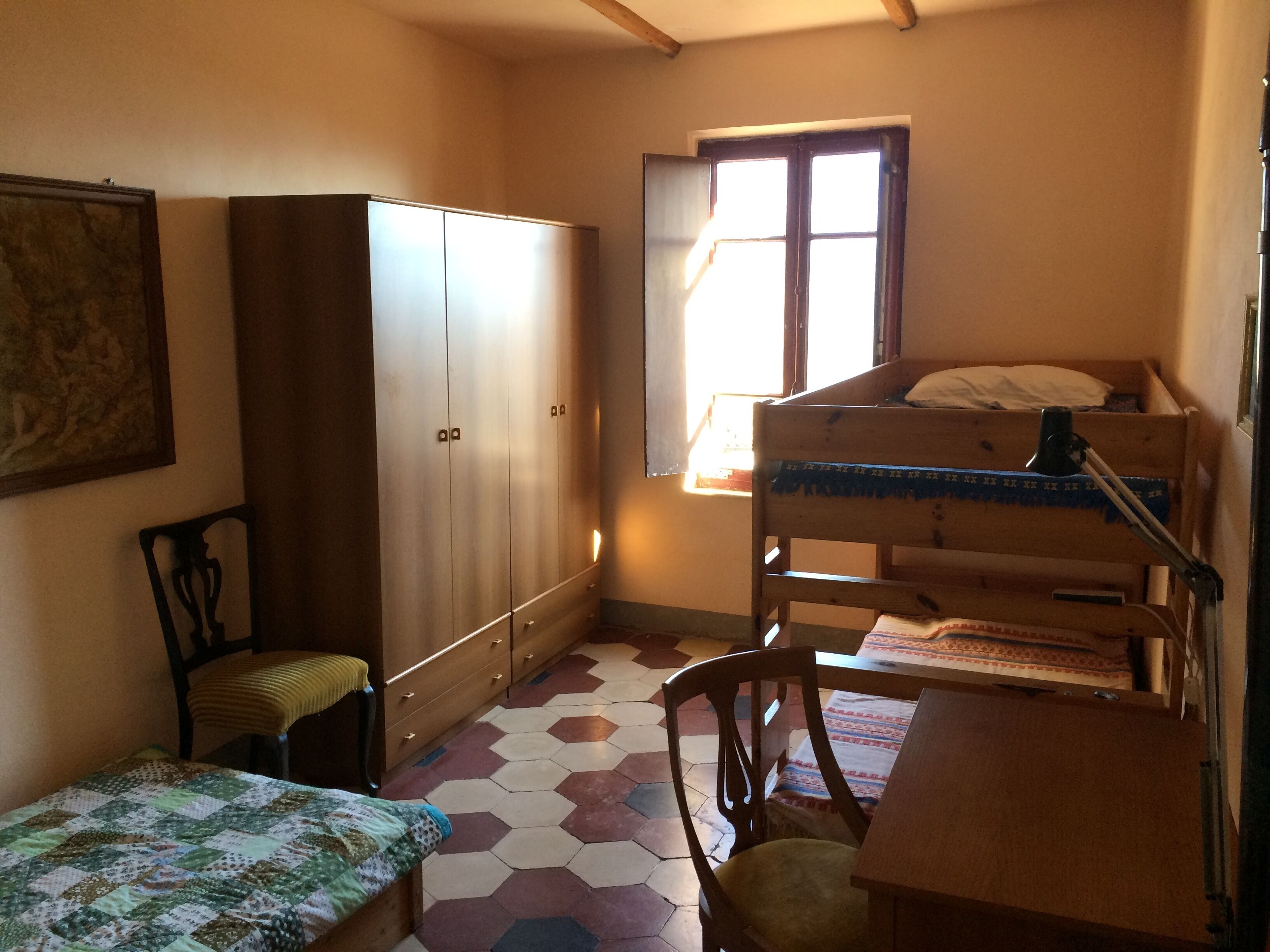 A small, compact room with a bunk bed, a wooden wardrobe, a single chair, and a small table.