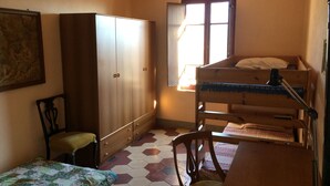 Een kleine, compacte kamer met een stapelbed, een houten garderobe, een enkele stoel en een klein tafeltje.