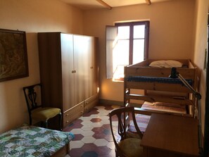 A small, compact room with a bunk bed, a wooden wardrobe, a single chair, and a small table.