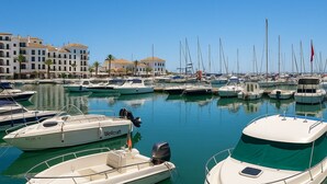 Un port de plaisance où sont amarrés différents types de bateaux, avec des bâtiments en arrière-plan et un ciel dégagé.