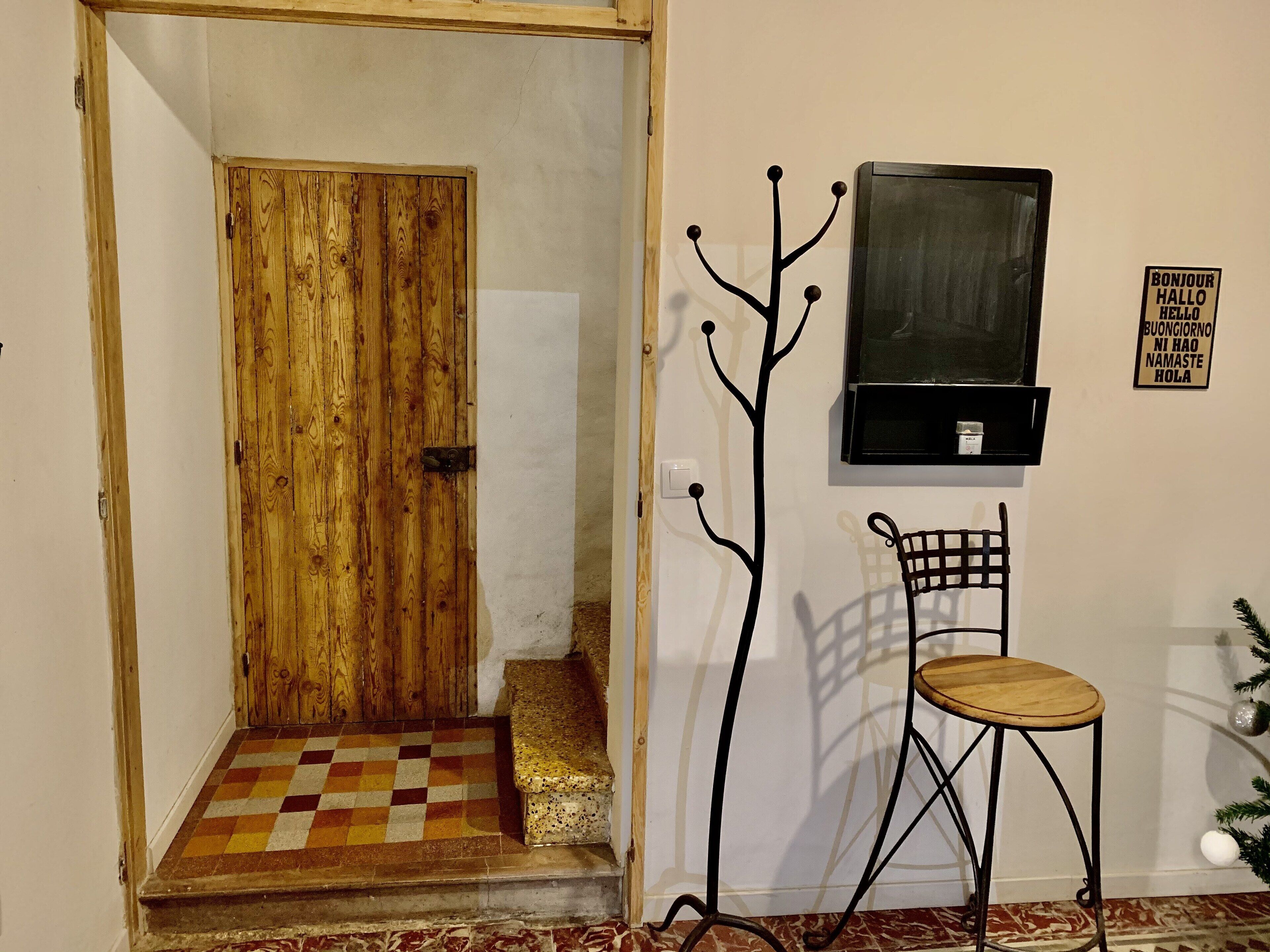 A wooden door leading to a room with a checkered floor, a wall-mounted TV, a metal coat rack, and a chair.