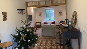 Een gezellige kamer met een kerstboom, een houten bankje, een klein tafeltje met een lantaarn en een raam met uitzicht op groen.