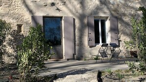 Un bâtiment rustique en pierre, doté de nombreuses fenêtres et portes, une allée en gravier et un espace extérieur aménagé pour s’asseoir.