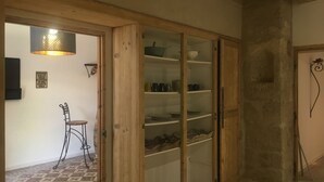 Een kamer met een houten deur die leidt naar een keuken, een kleine tafel met een stoel, en een bord aan de muur met begroetingen in verschillende talen.