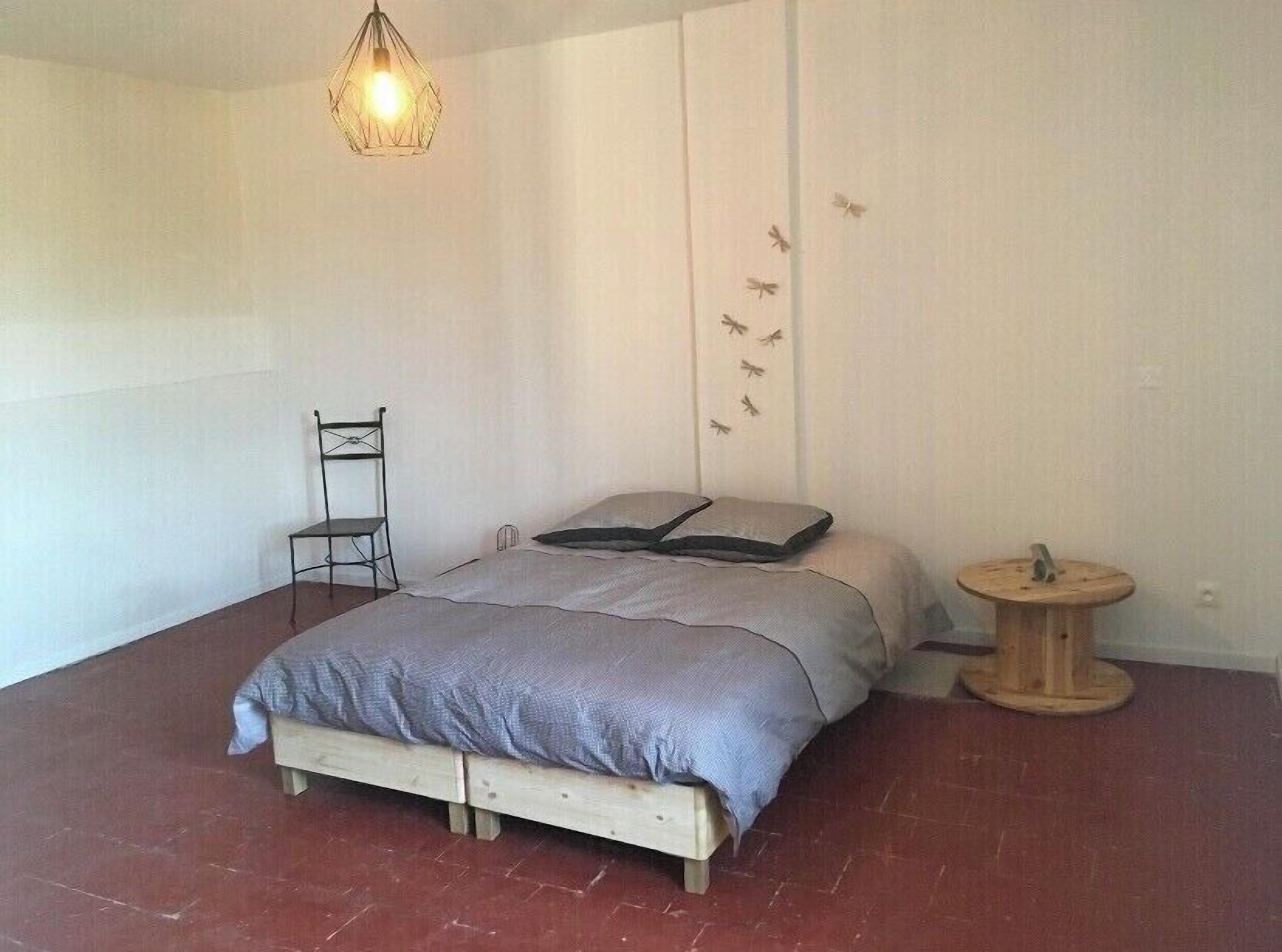 A bedroom with a bed, a chair, a small round table, and a wall with a light fixture and a wall decal of birds.