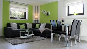 A modern living room with a grey sofa, a glass coffee table, and a dining area with four chairs and a table.
