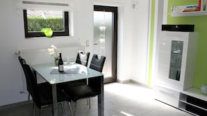 A dining area with a glass table, black chairs, a vase with flowers, and a window with a view of greenery.