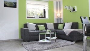 A modern living room with a grey sofa, a glass coffee table, and a fluffy rug.