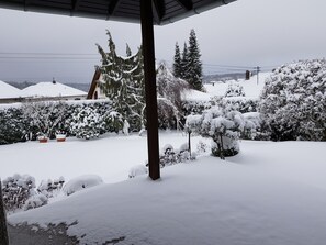 Un jardín cubierto de nieve con plantas en macetas y una pérgola de madera.