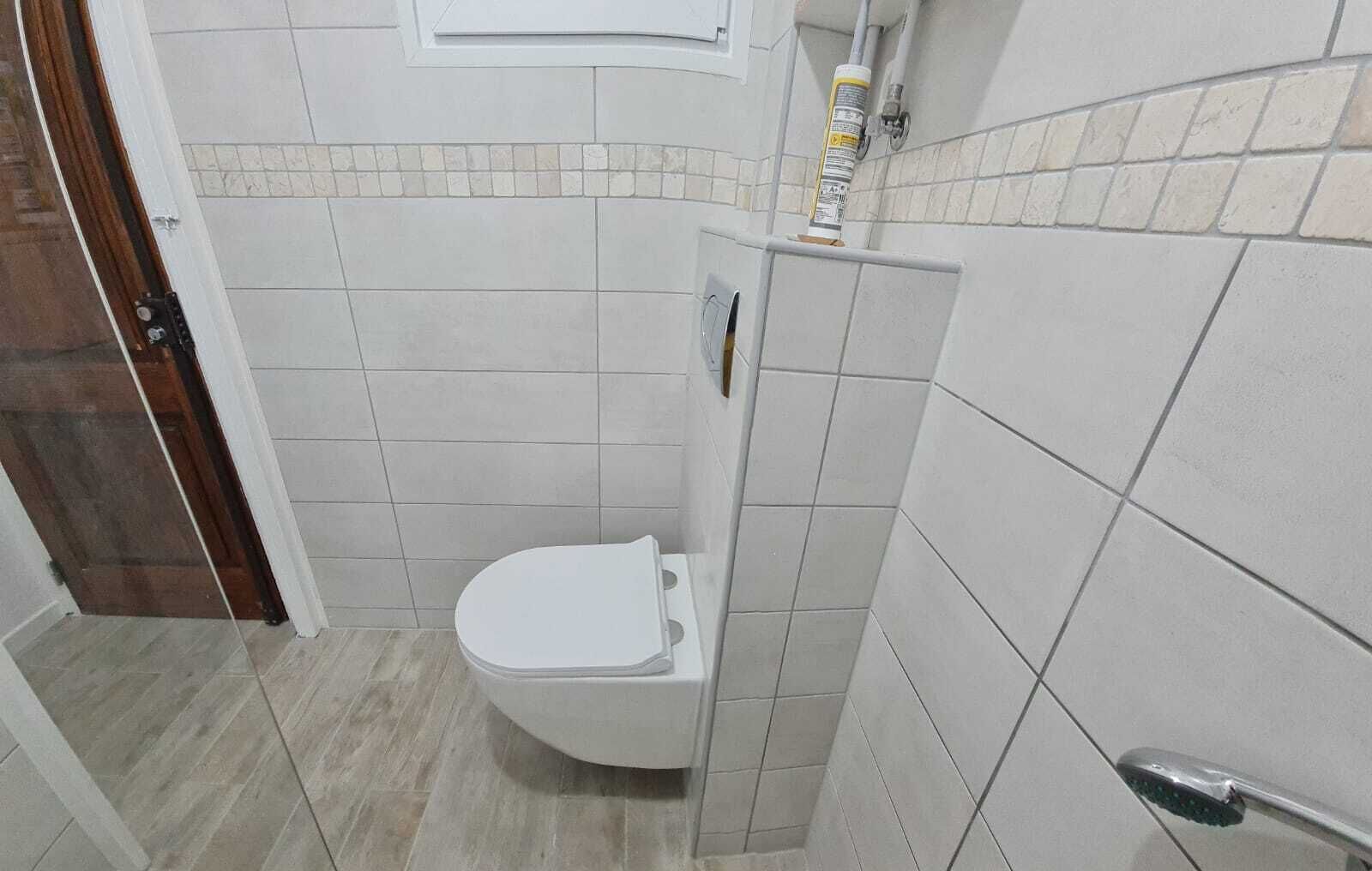 Uma casa de banho pequena com sanita, zona de duche e pavimento em mosaico.