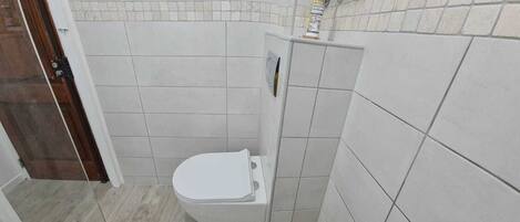 Uma casa de banho pequena com sanita, zona de duche e pavimento em mosaico.