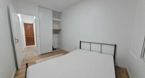 Une chambre à coucher comprenant un lit, une armoire et une porte donnant sur une autre pièce.