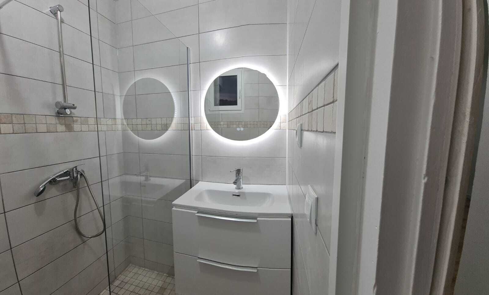 A bathroom with a shower, two sinks, and two round mirrors.