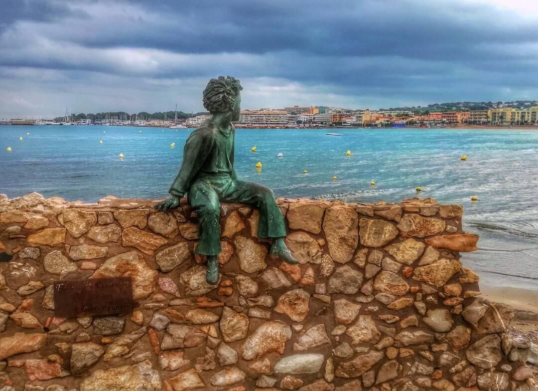 A statue of a seated figure on a stone wall by a body of water.