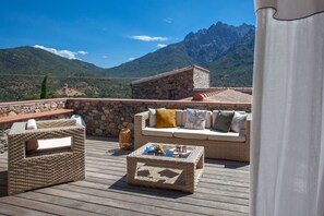 Una terraza con mobiliario de mimbre, un muro de piedra y vistas a la montaña.