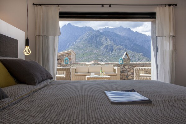A bedroom with a bed, a nightstand, and a view of mountains through a window.