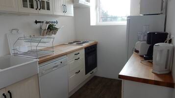 A compact kitchen with white cabinets, a wooden countertop, a dishwasher, an oven, and a coffee maker.
