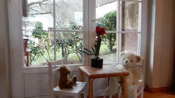 A room with a large window, a small table, two chairs, and a teddy bear.