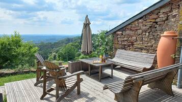 A wooden deck with a bench, chairs, and a table set for dining, overlooking a scenic landscape.