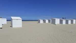 A row of white, rectangular structures on a sandy beach with a clear blue sky.