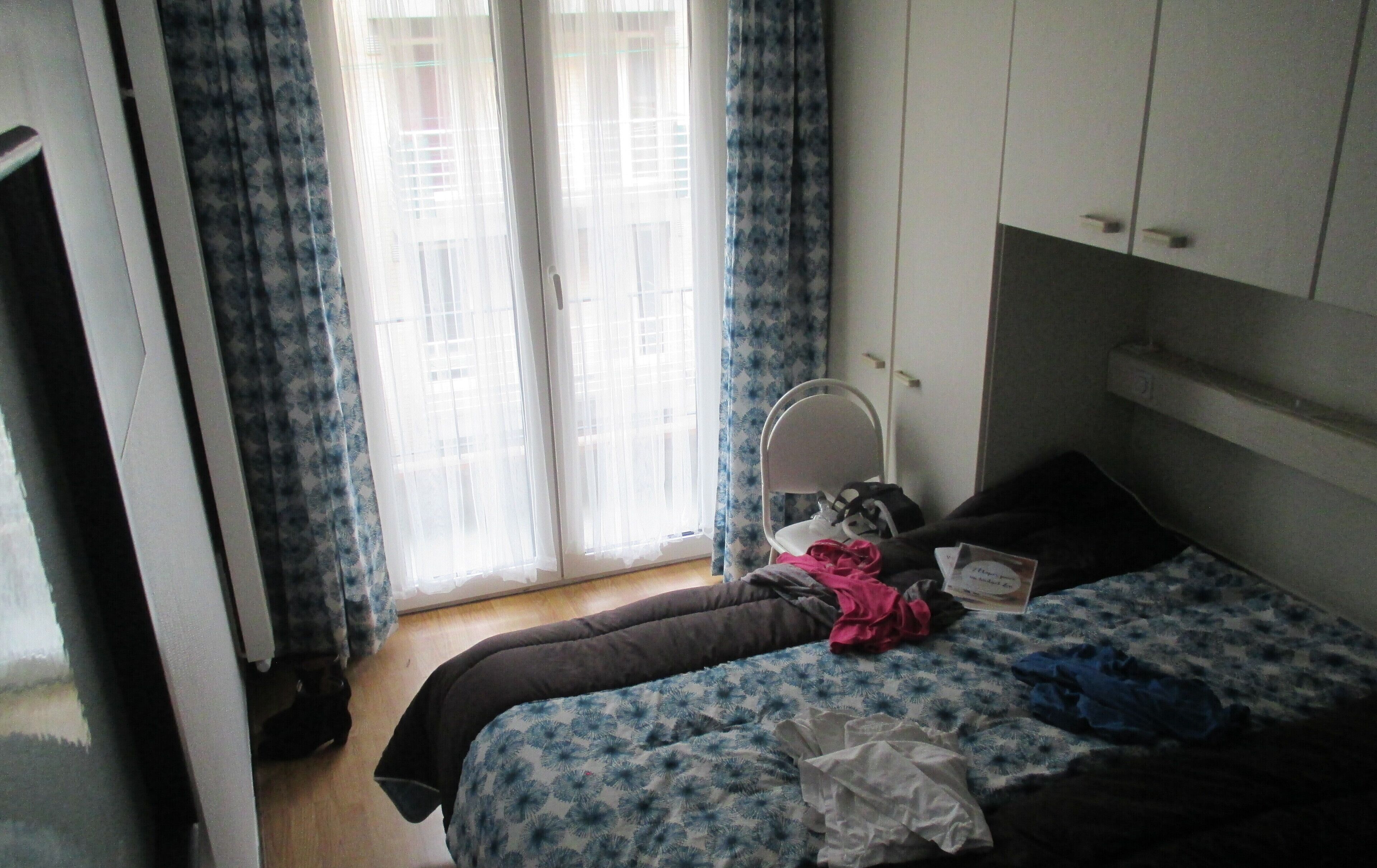 A bedroom with a bed, a chair, a mirror, and a window with curtains.